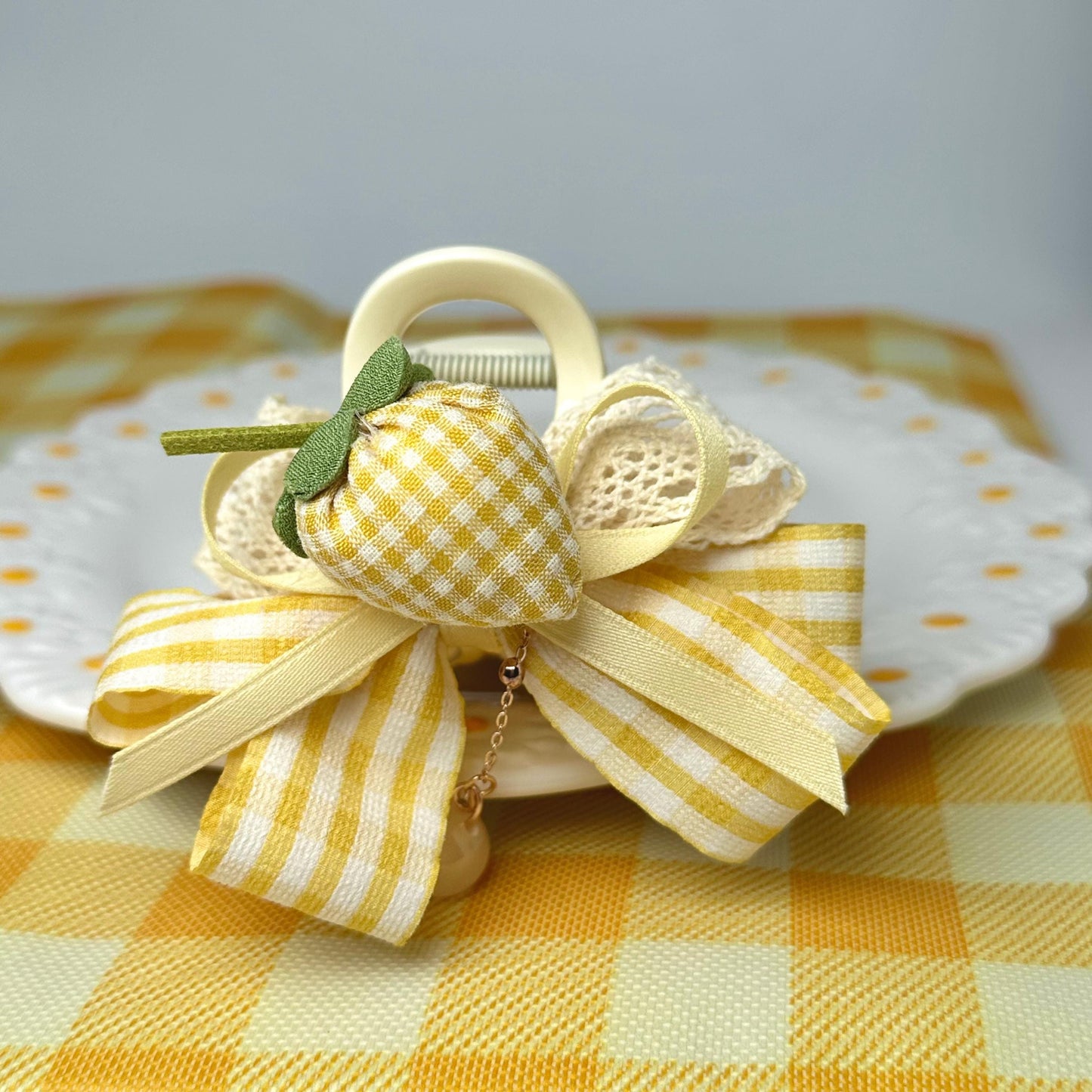 A decorative bow made of fabric and ribbons, featuring a yellow and white checkered pattern, is placed on a white plate with a yellow and white checkered tablecloth.