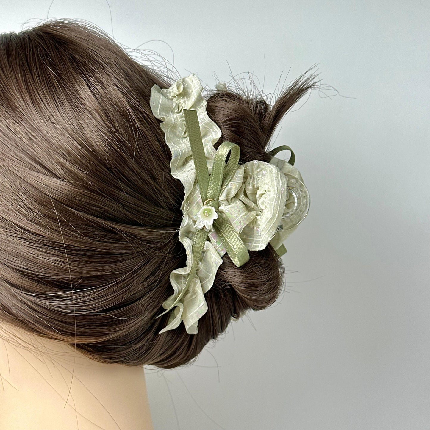 A close-up view of a woman's hair with a decorative hair accessory featuring a white flower and green ribbon.