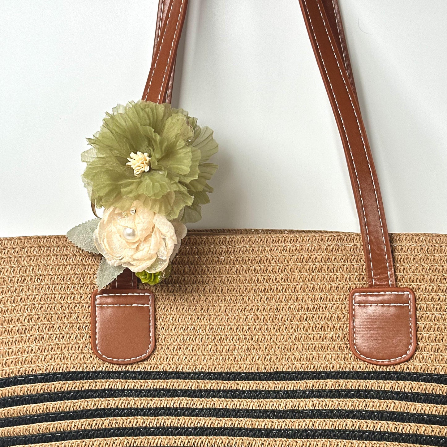 A straw bag with a green flower attached to the handle.