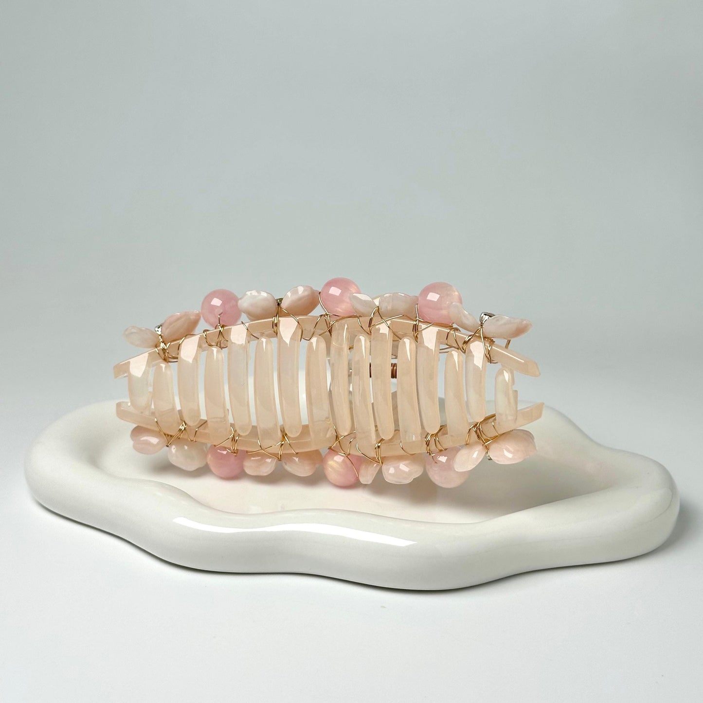 A white ceramic plate with a decorative hair accessory made of small, colorful beads and wire.