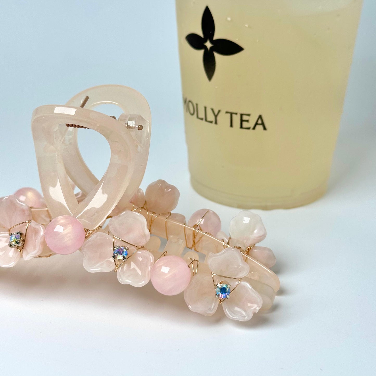 A close-up image of a hair clip with pink flower-shaped charms and a cup of tea with a logo on it.