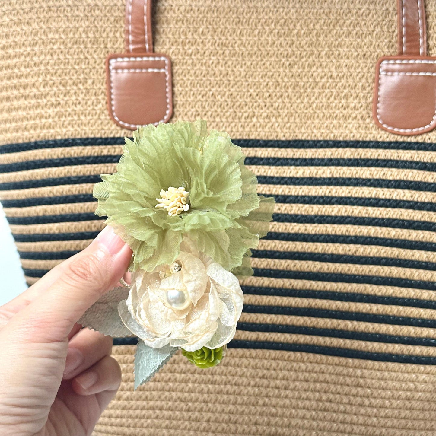 A hand holding a green flower with a white center, against a background of a striped bag.