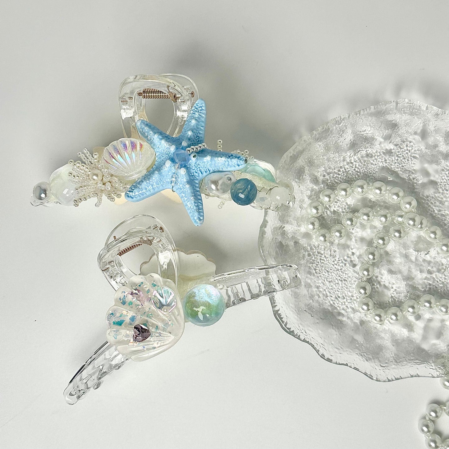 a collection of clear hair clips adorned with various seashells, pearls, and starfish, creating a nautical-inspired design.