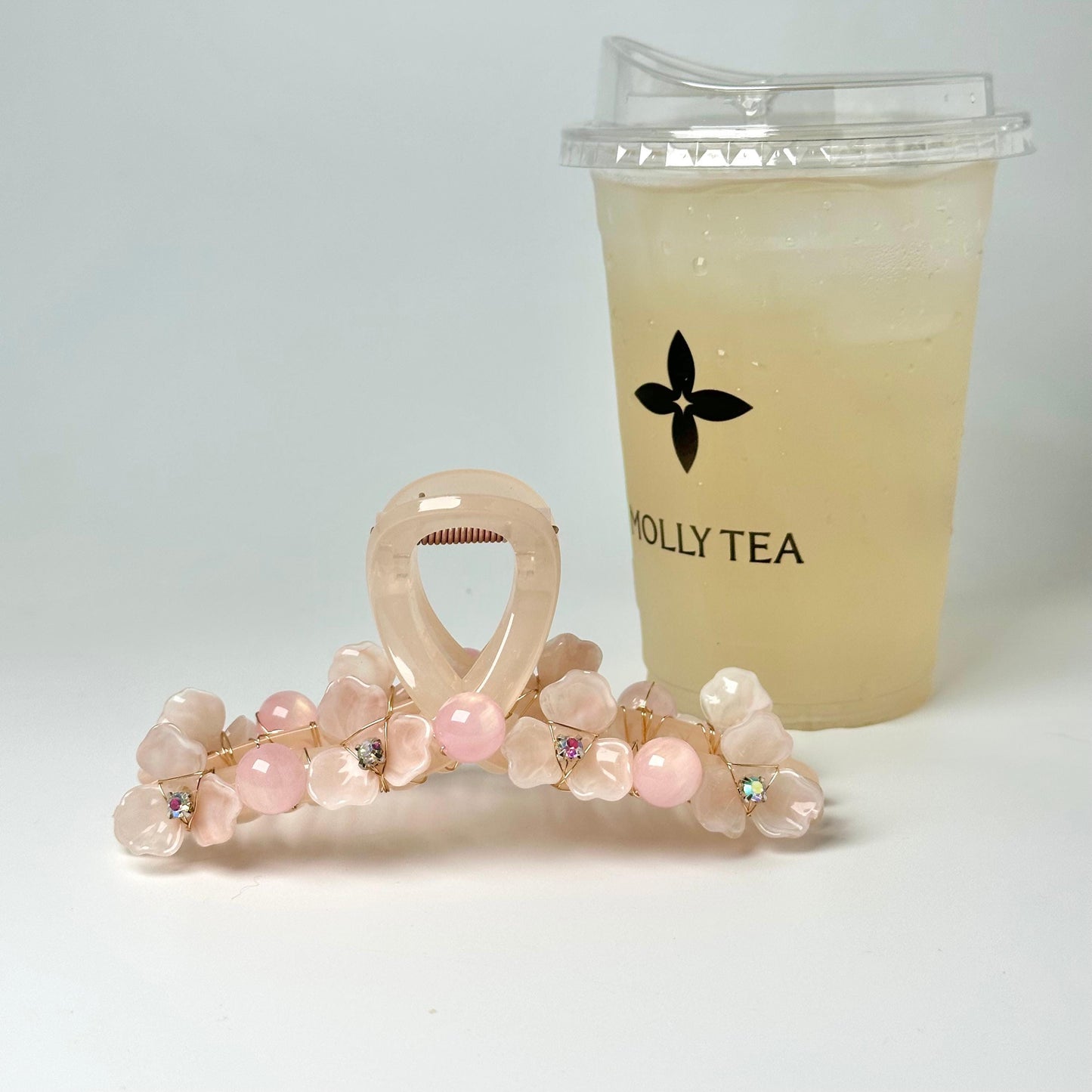 a pink hair clip adorned with pink flowers and a cup of tea with a logo on it, placed on a white surface.