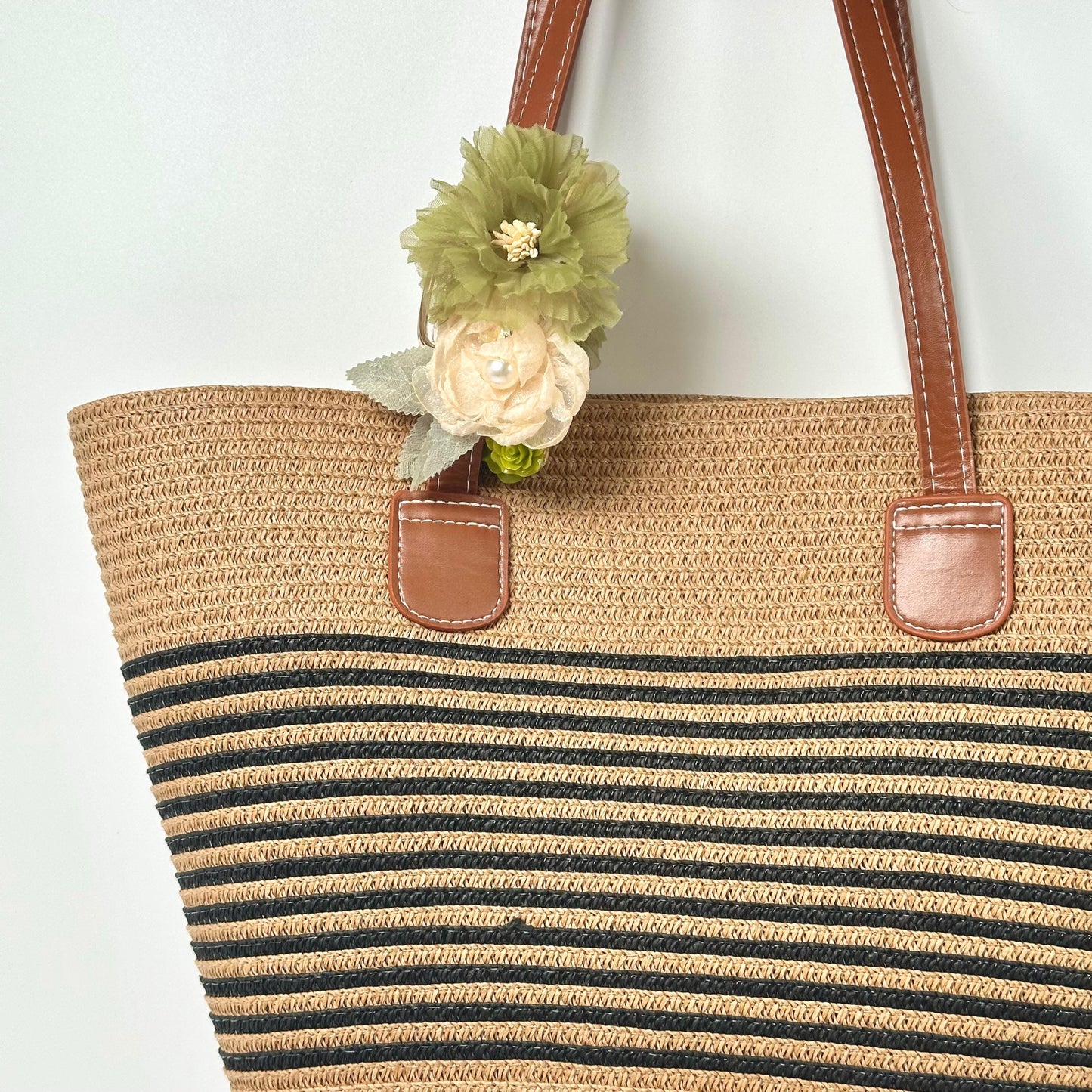 A beige and black striped tote bag with a single green flower attached to the handle.