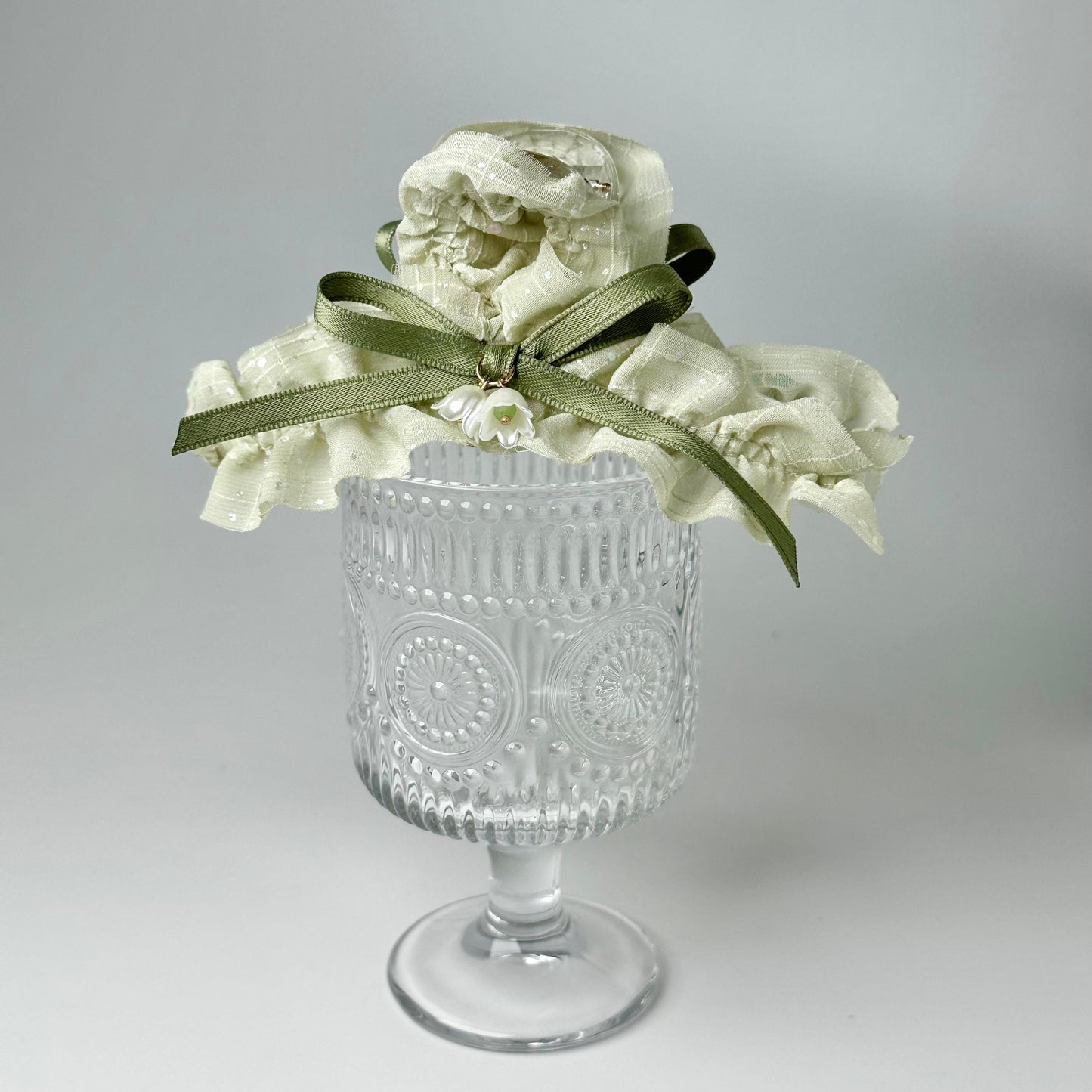 A clear glass vase with a white flower arrangement on top, placed on a white surface.