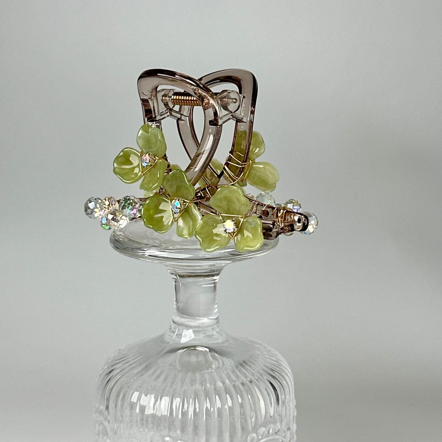 A clear glass vase with a decorative green and silver floral arrangement on top.