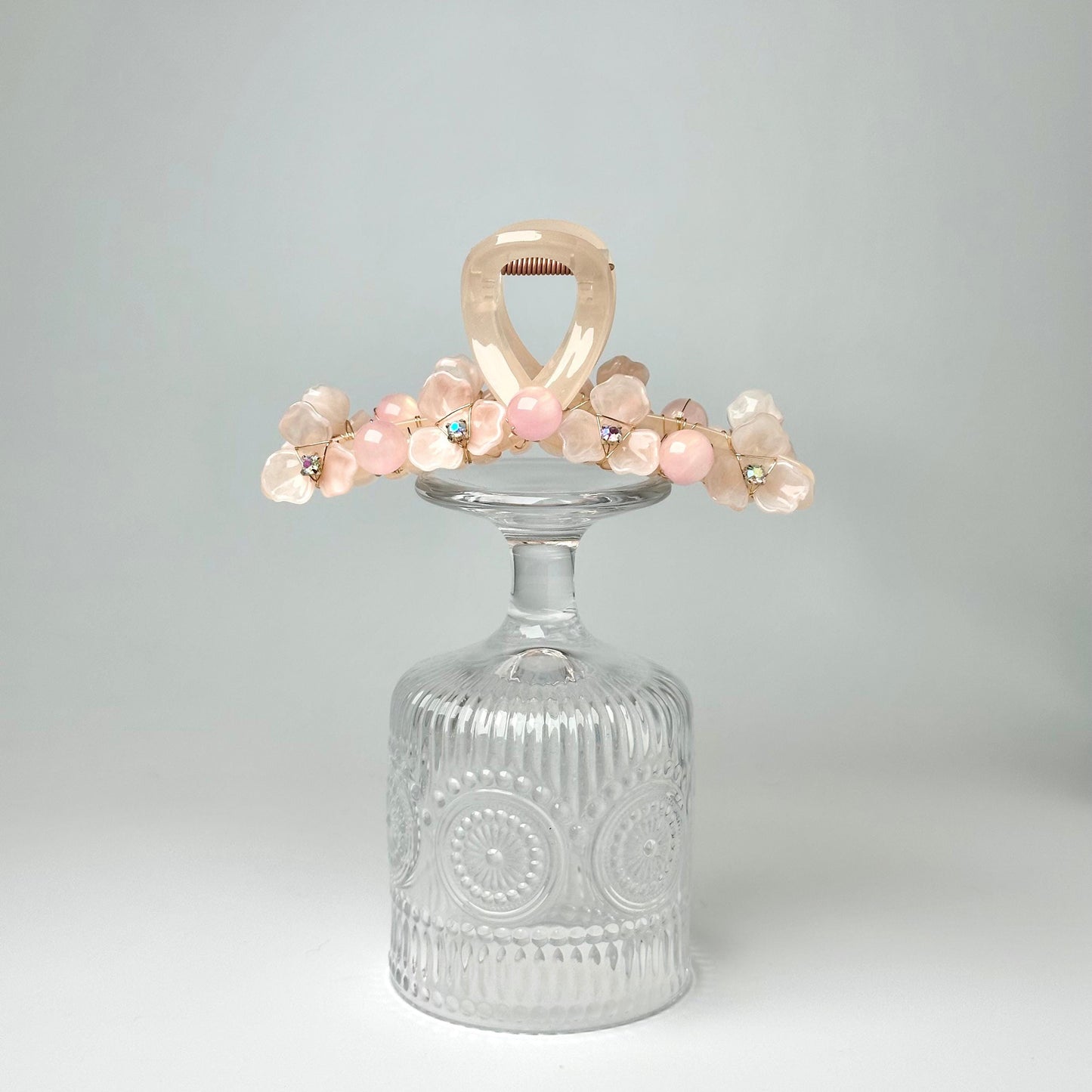 A clear glass vase with a floral arrangement on top, placed on a white surface against a light background.
