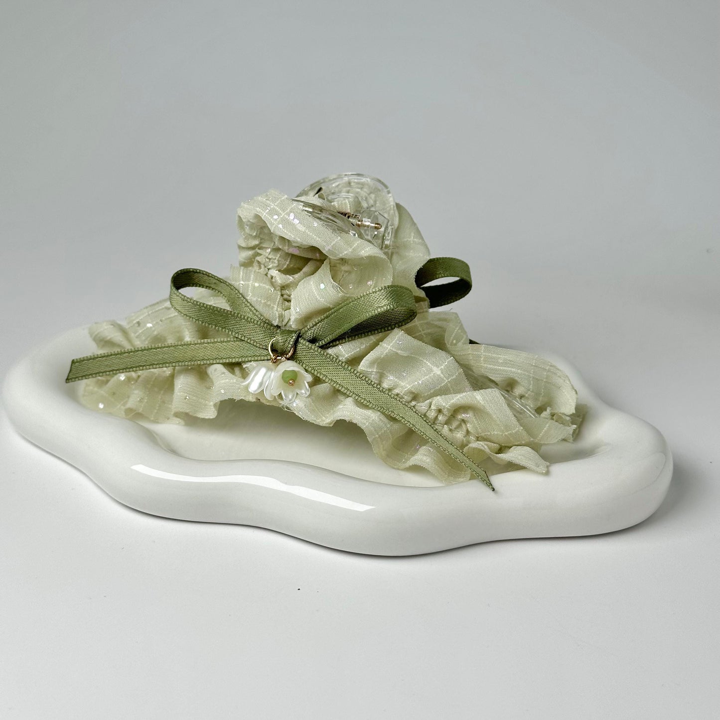A white ceramic plate with a green ribbon and a small white flower decoration on it.