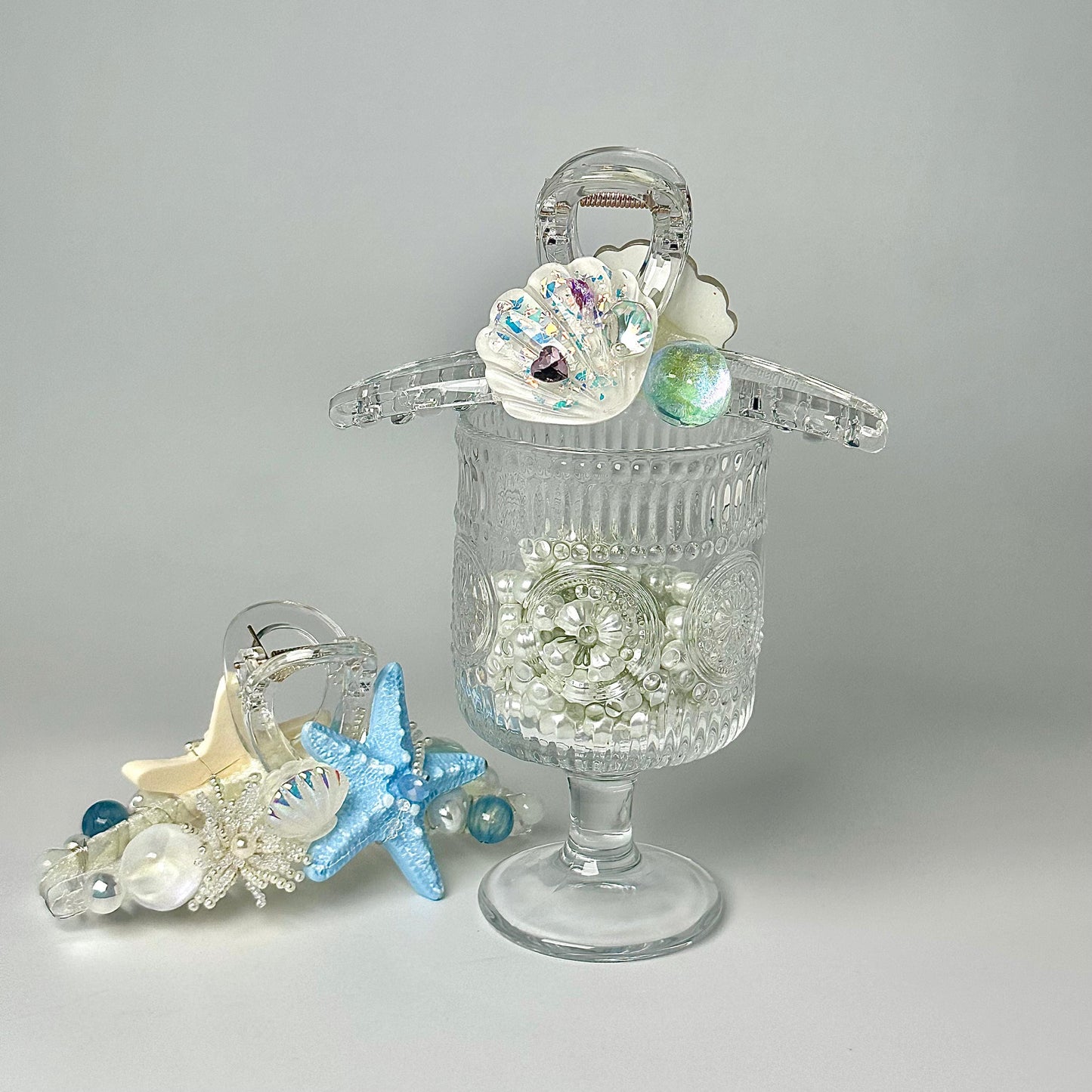 a clear glass vase with a seashell and a starfish on top, along with a clear glass container holding small white and blue beads.