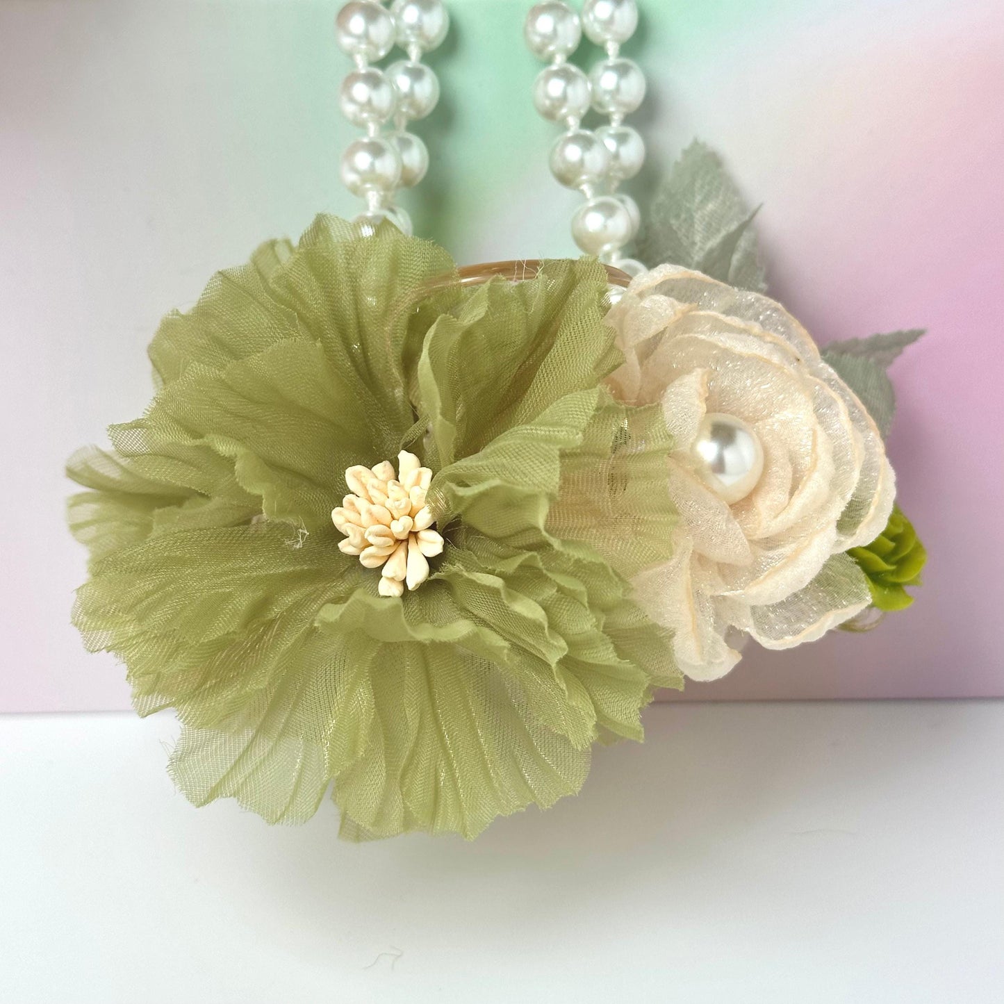 A green and white flower-shaped purse with a pearl accent, hanging against a pink background.