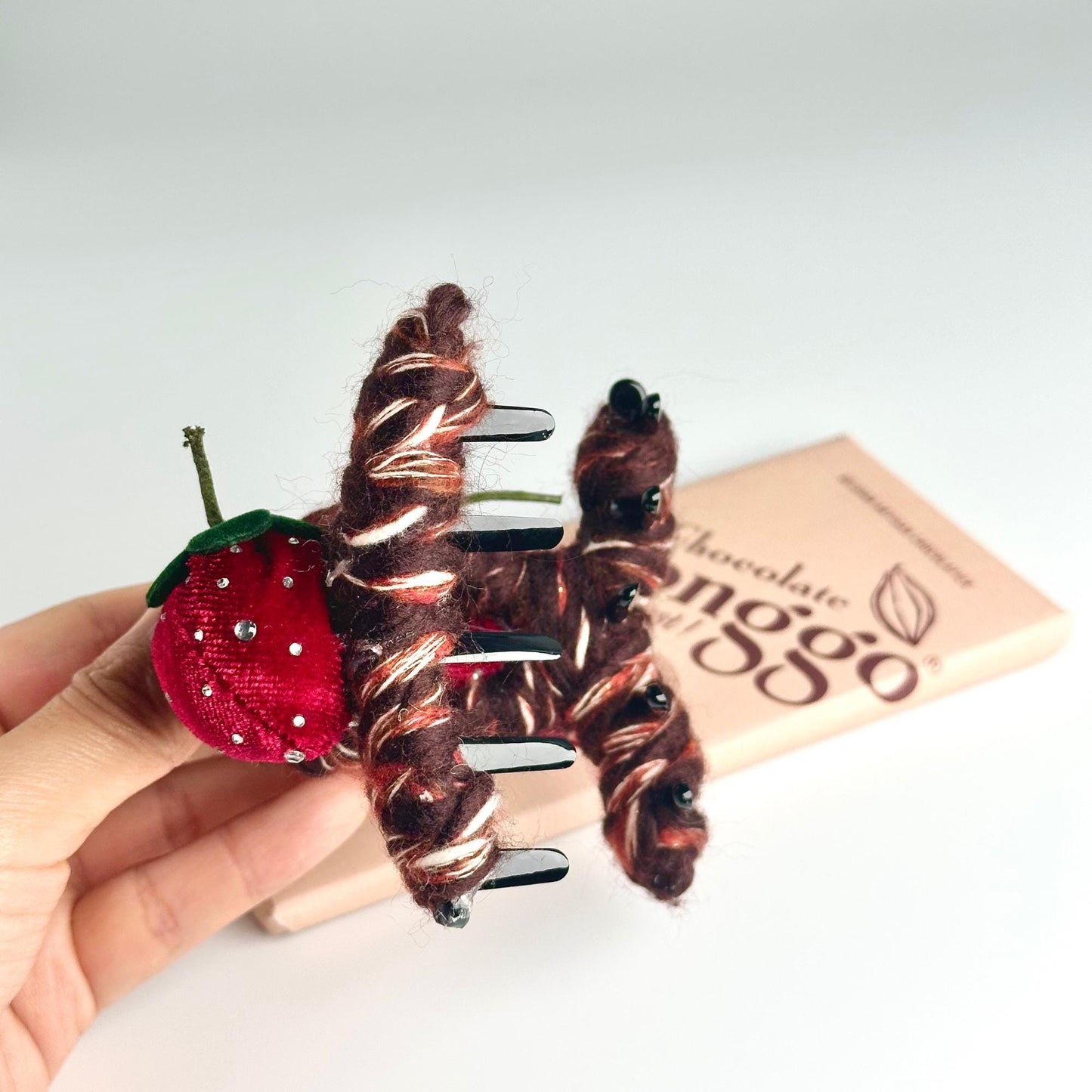 a person is holding a small doll with a strawberry on it