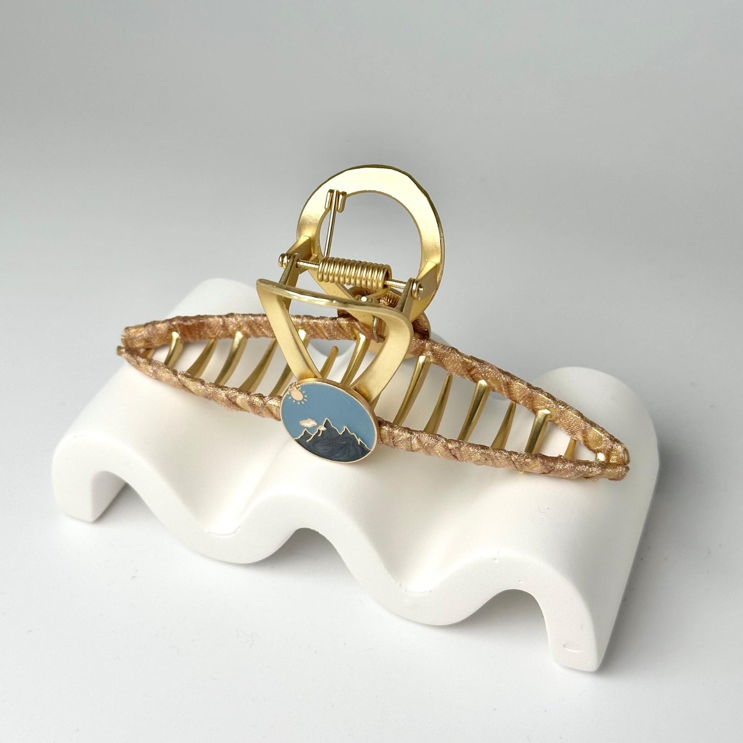 a gold and blue brooch sitting on top of a white stand