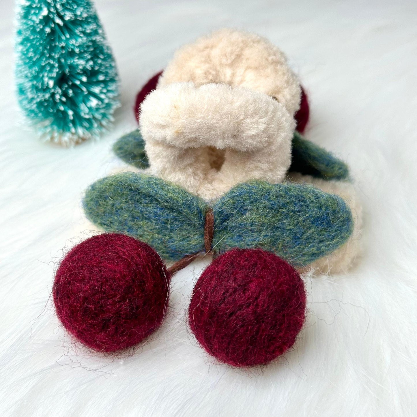 a teddy bear with two balls of yarn next to a christmas tree