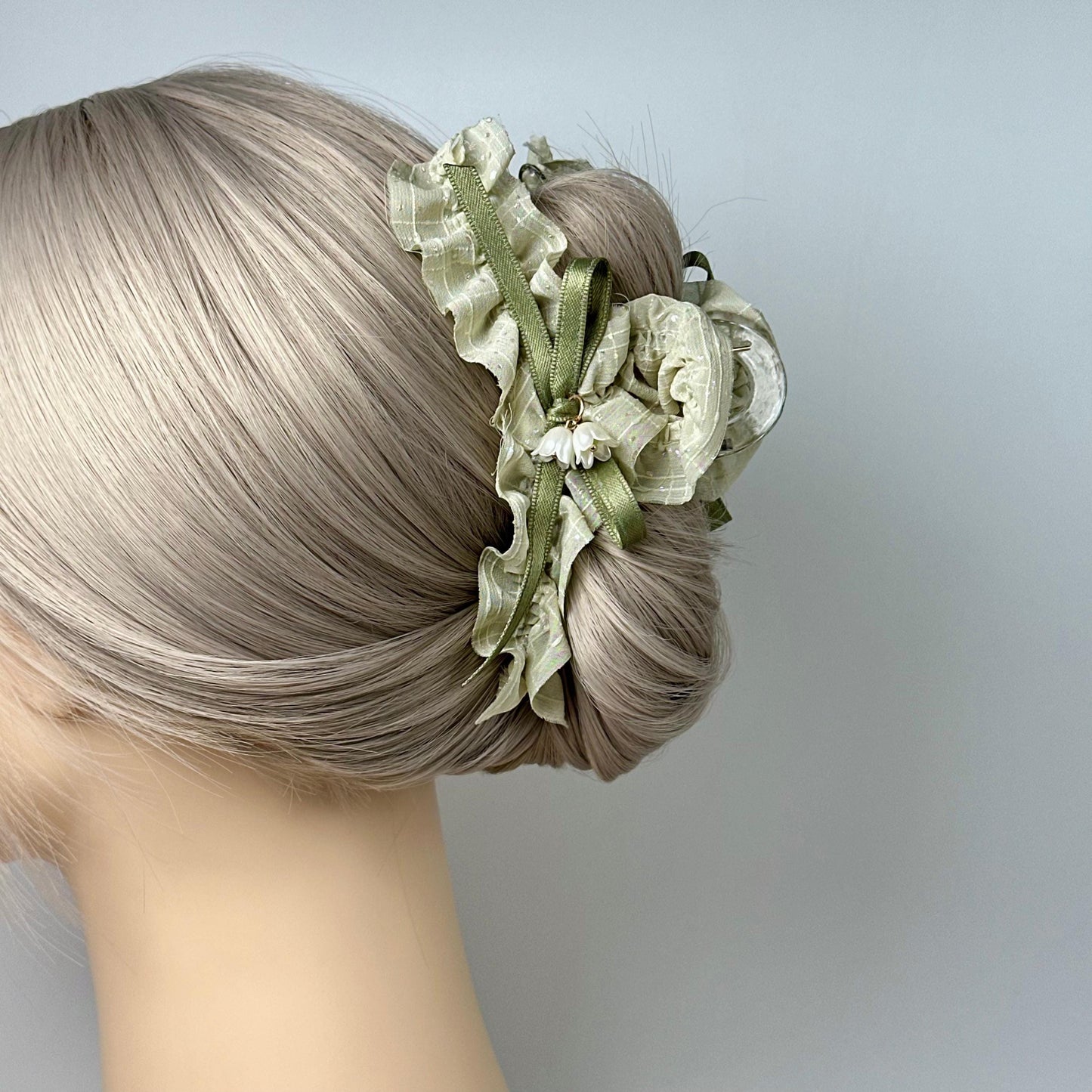 A close-up of a woman's blonde hair with a decorative hair clip featuring a white flower and green ribbon.