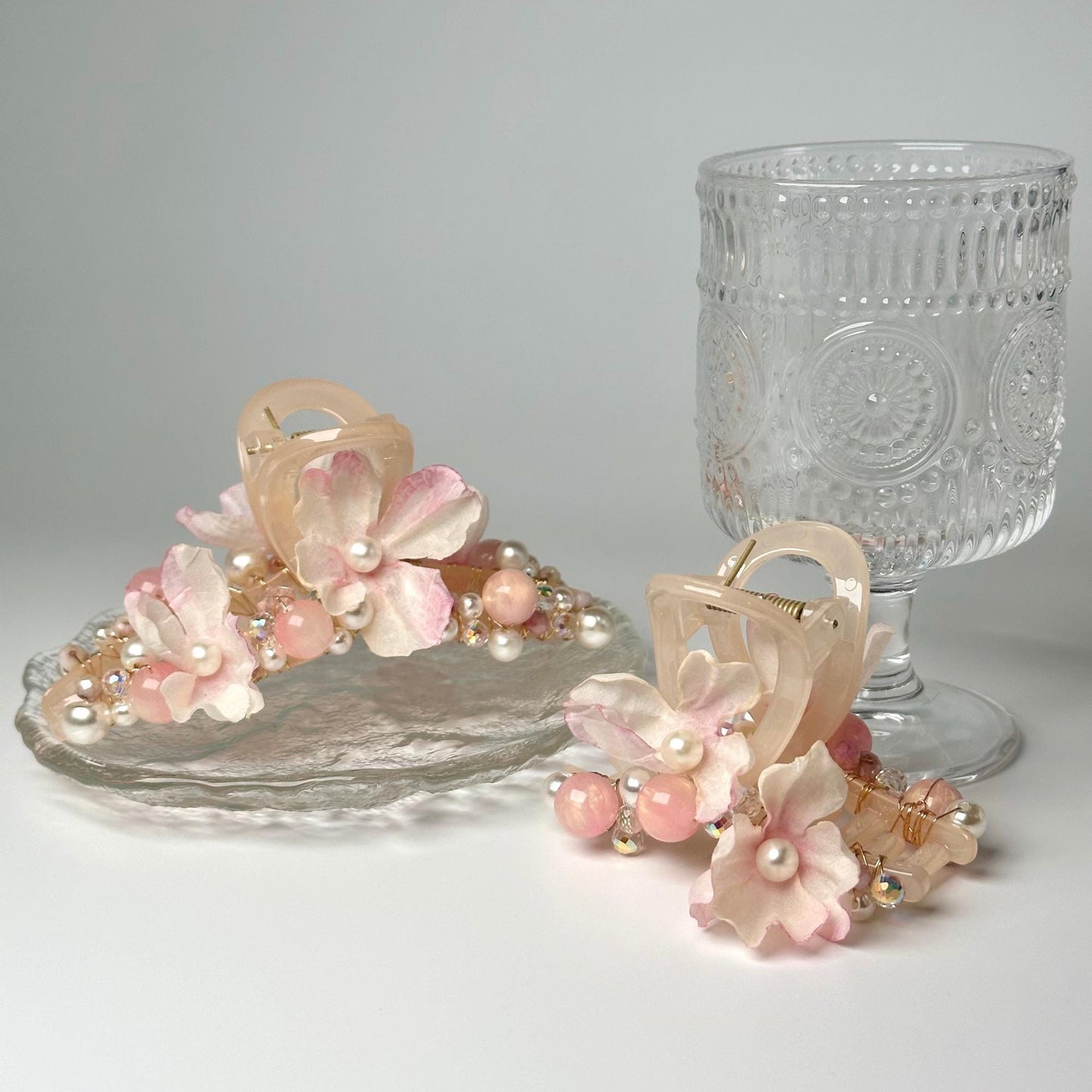 a pair of pink flowers and pearls sit next to a glass