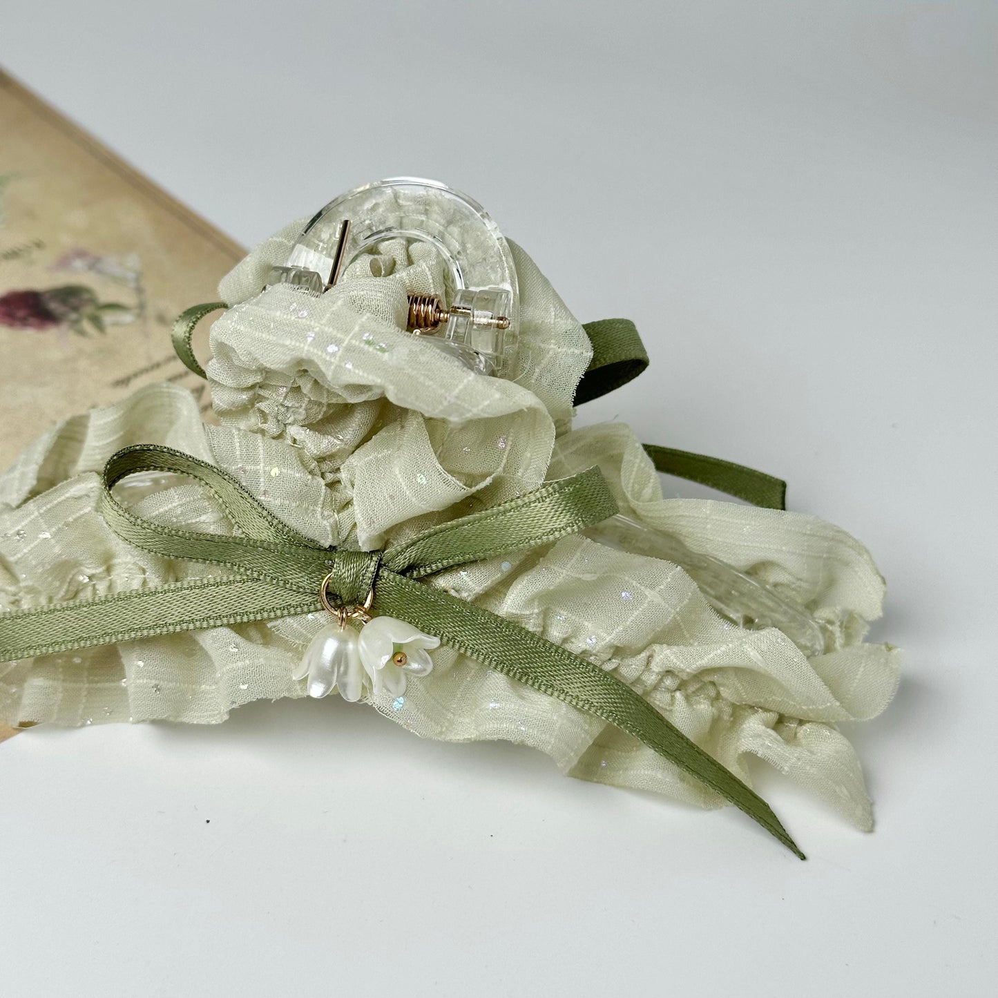 A decorative headband with a green ribbon and a clear bead, possibly made of glass or crystal, is displayed on a white surface.