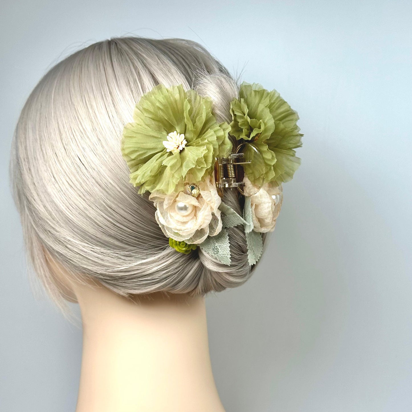 A mannequin head with a woman's blonde hair styled in a bun, adorned with a green flower clip and a white flower.
