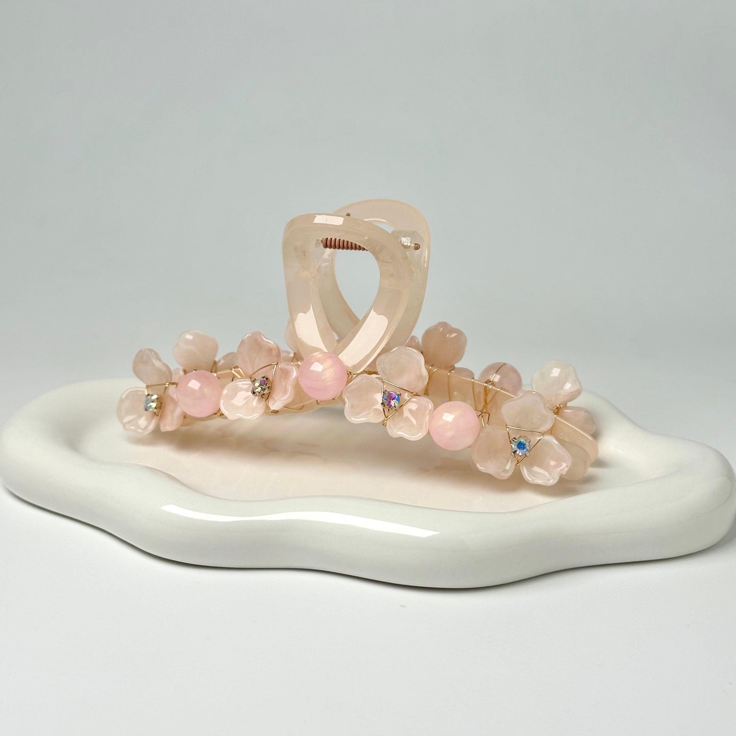 A white ceramic plate with a floral hair clip and a pair of hair clips adorned with pink flowers.