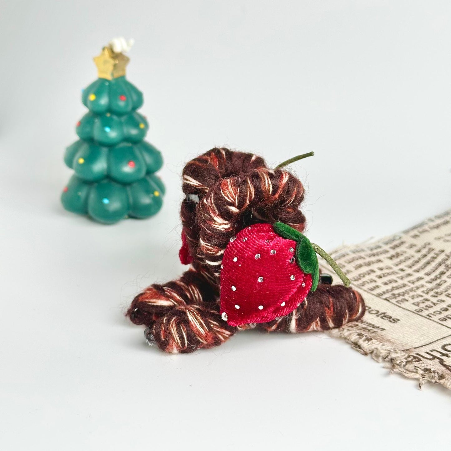 a small stuffed strawberry sitting next to a small christmas tree