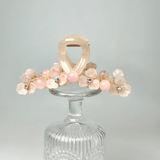 A glass vase with a floral arrangement of pink and white flowers and small, round stones or beads on top.