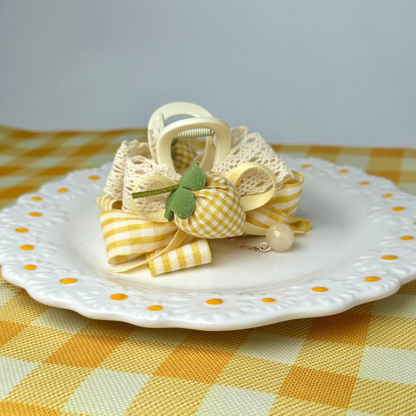 A decorative plate with a yellow and white checkered pattern, featuring a bow made of fabric and ribbons, and a small white charm.