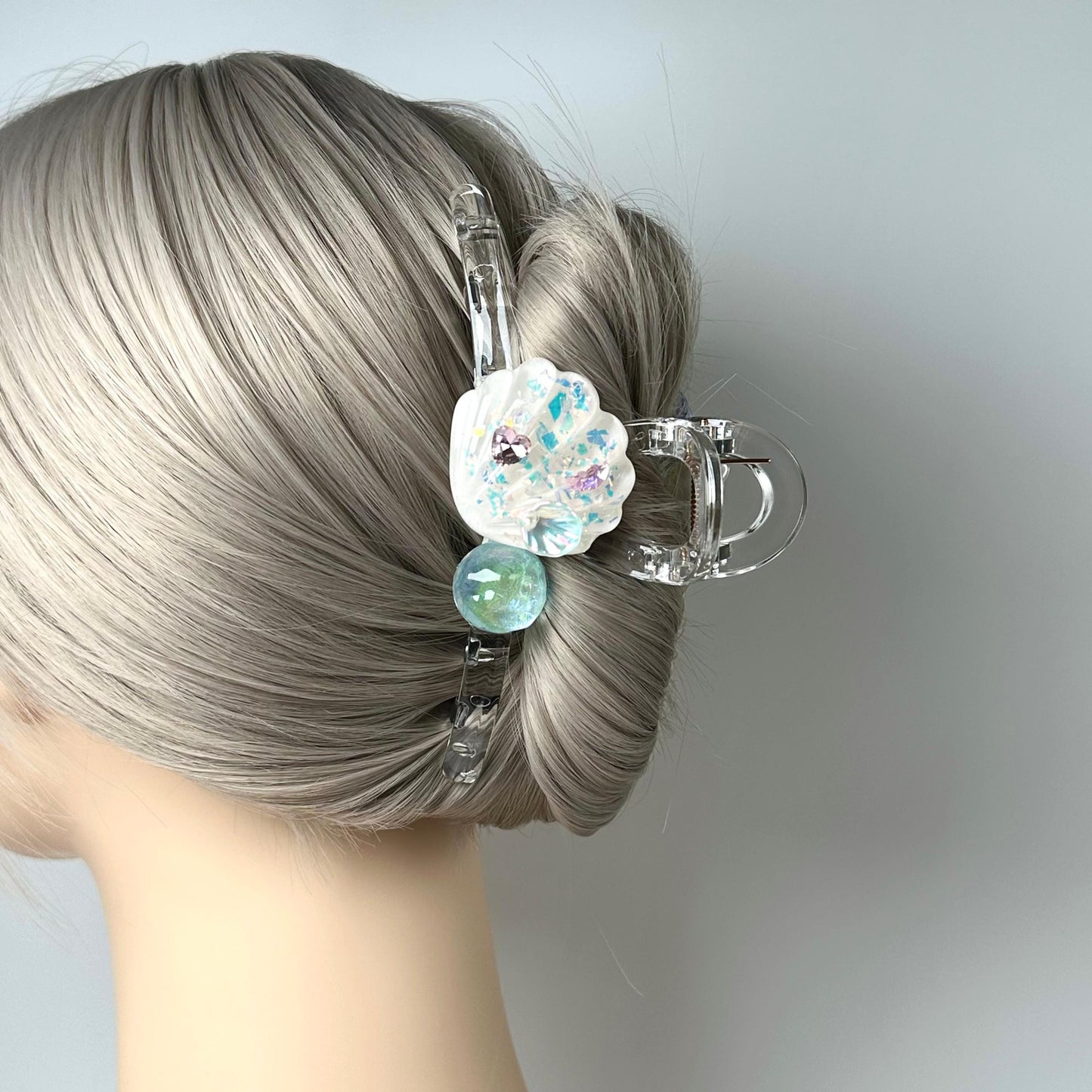 A close-up view of a person's head with a hair clip featuring a flower design and a small green ball.