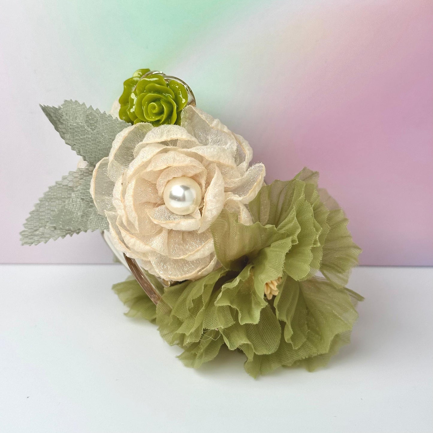 A white flower with a pearl at the center, surrounded by green leaves, is displayed against a pink and green gradient background.