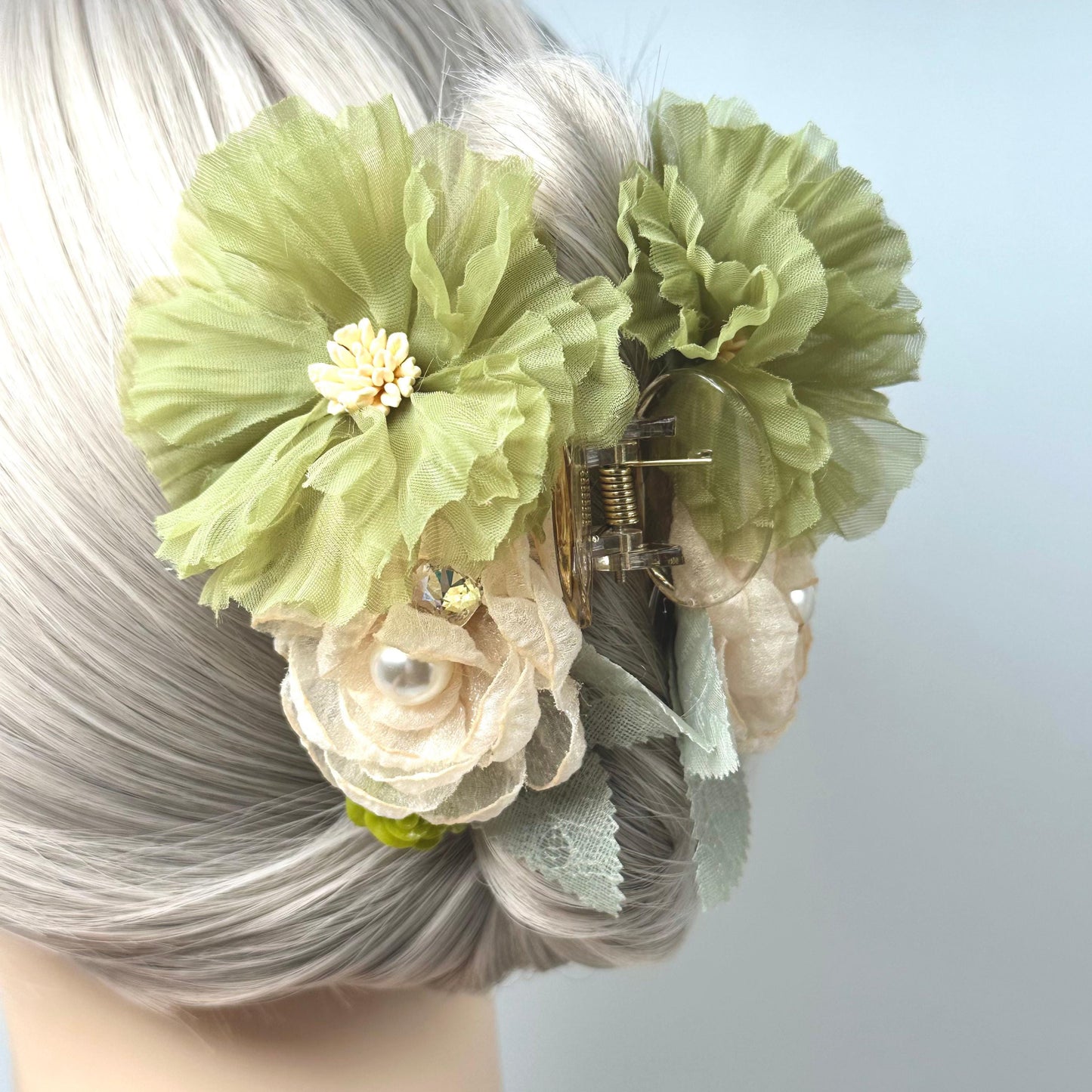 A close-up of a person's hair with a green flower clip adorned with white and beige flowers.