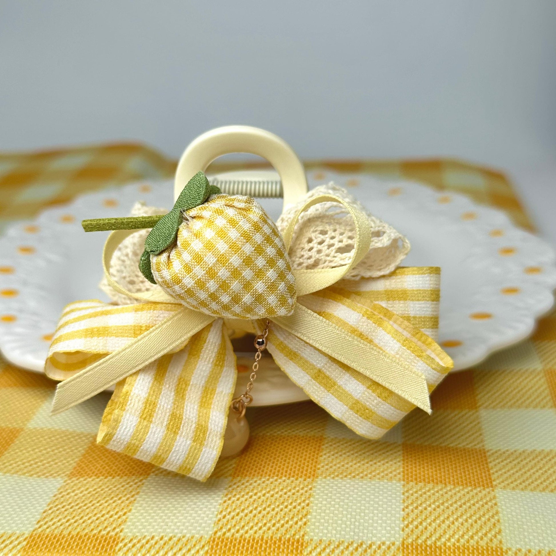 A decorative bow made of fabric and ribbons, featuring a yellow and white checkered pattern, is placed on a white plate with a yellow and white checkered tablecloth.