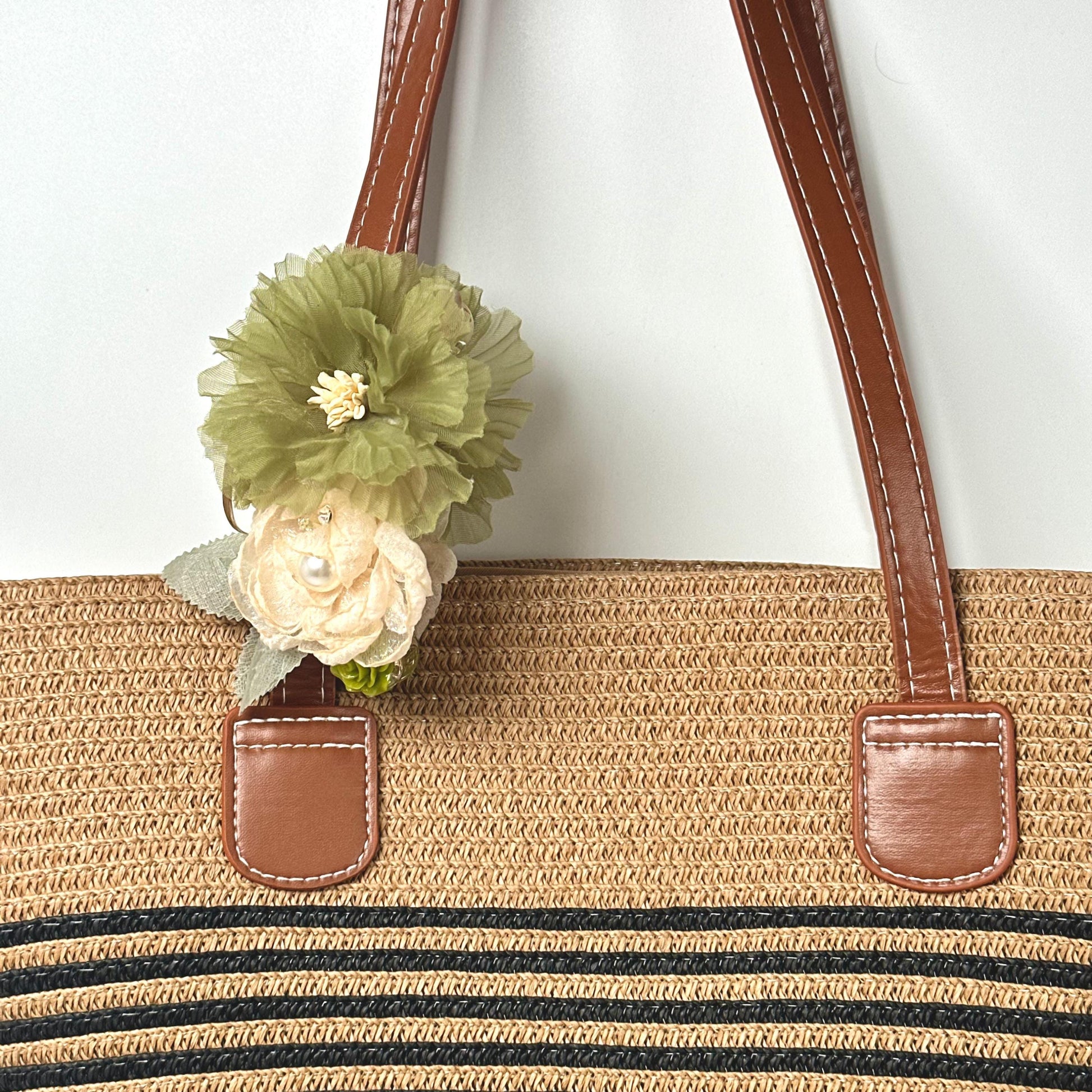A straw bag with a green flower attached to the handle.