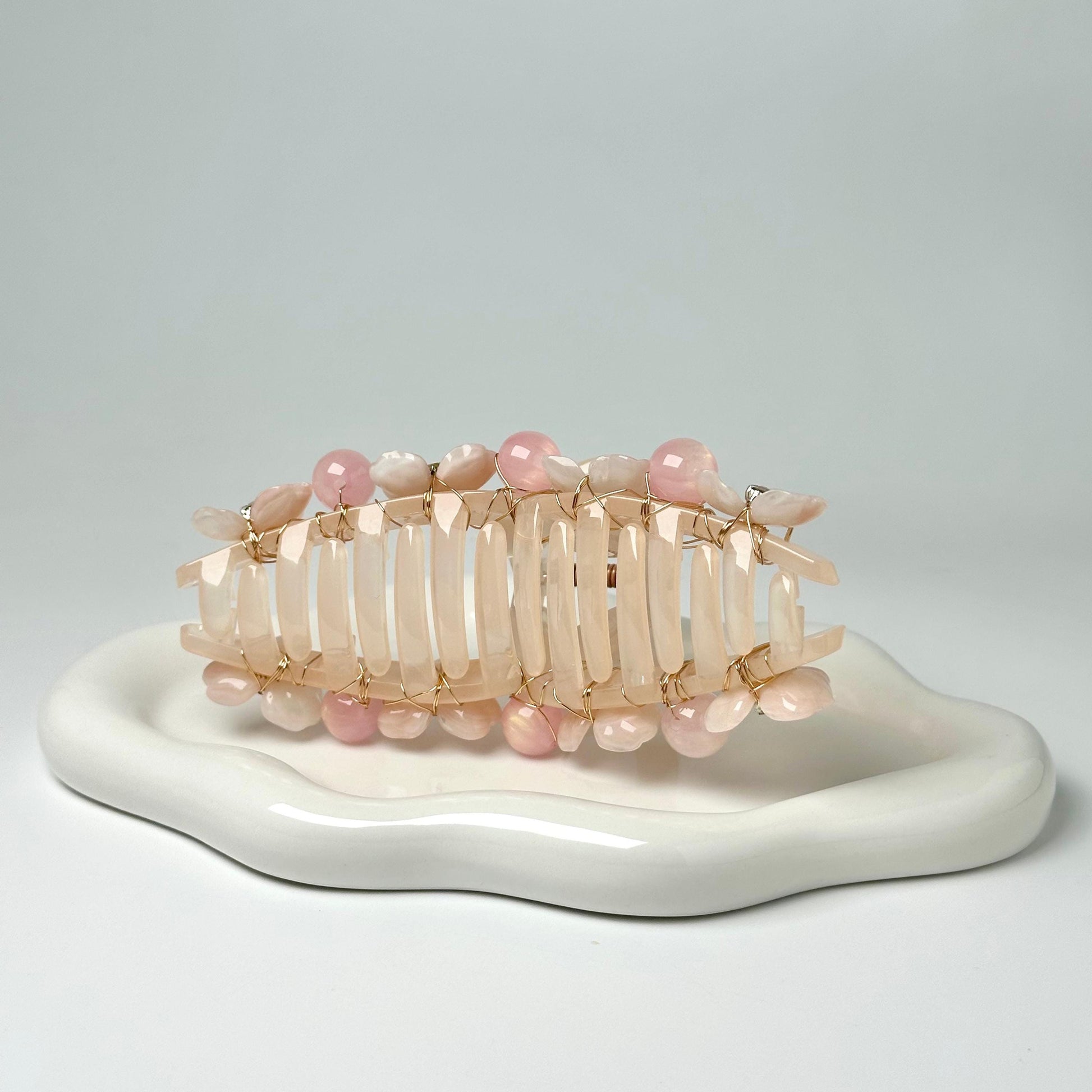 A white ceramic plate with a decorative hair accessory made of small, colorful beads and wire.