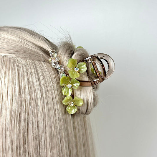 A close-up view of a blonde woman&#39;s hair with a decorative hair clip featuring green and clear gemstone elements.