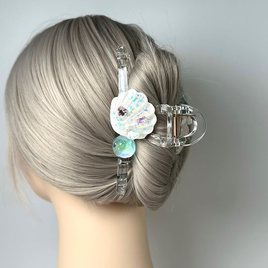 A close-up of a person&#39;s head with a clear plastic hair clip adorned with a shell-shaped charm and a round bead.