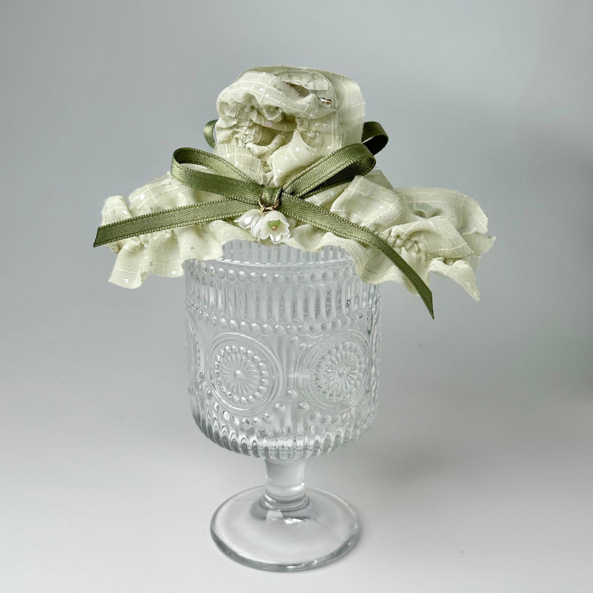 A clear glass vase with a white flower arrangement on top, placed on a white surface.