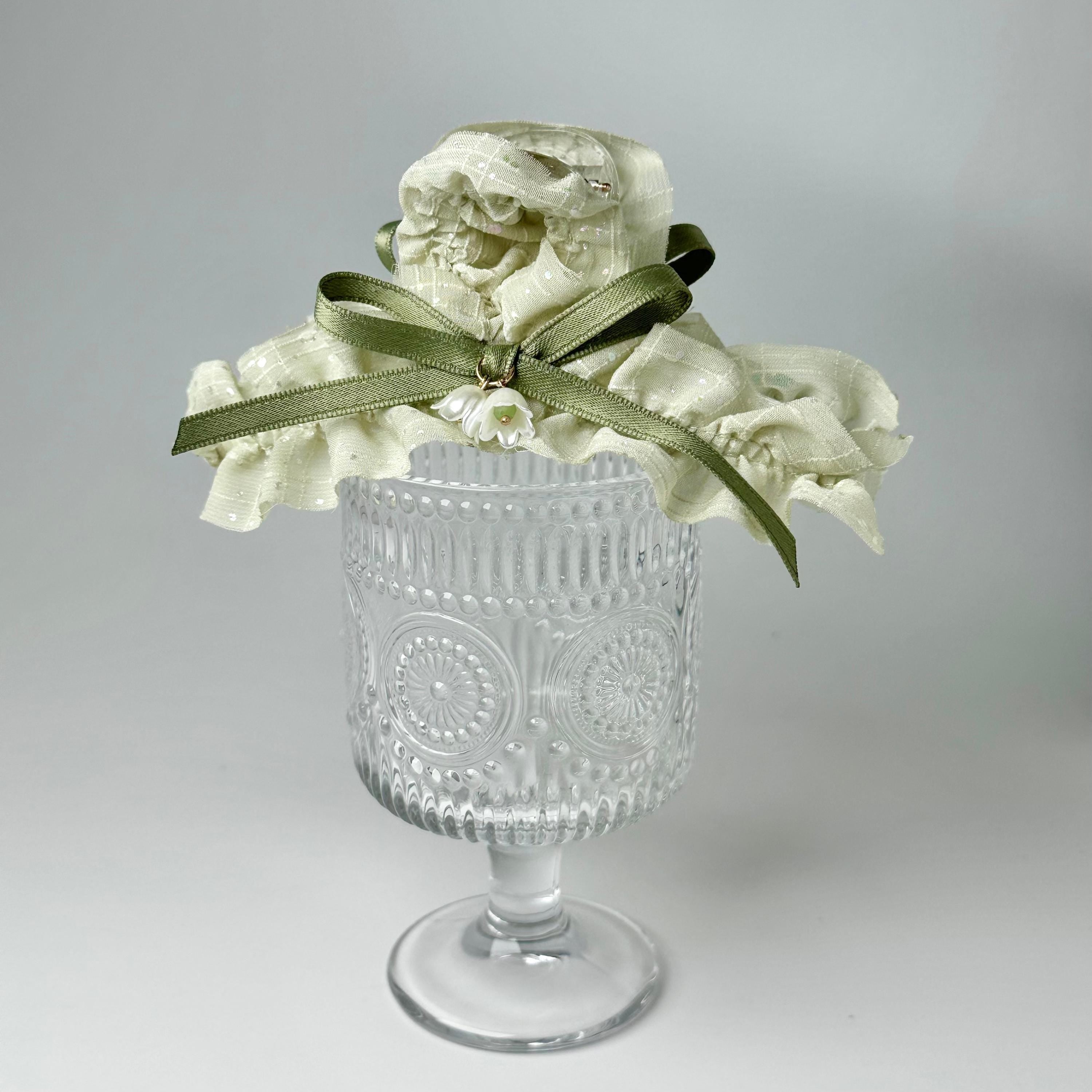 A clear glass vase with a white flower arrangement on top, placed on a white surface.