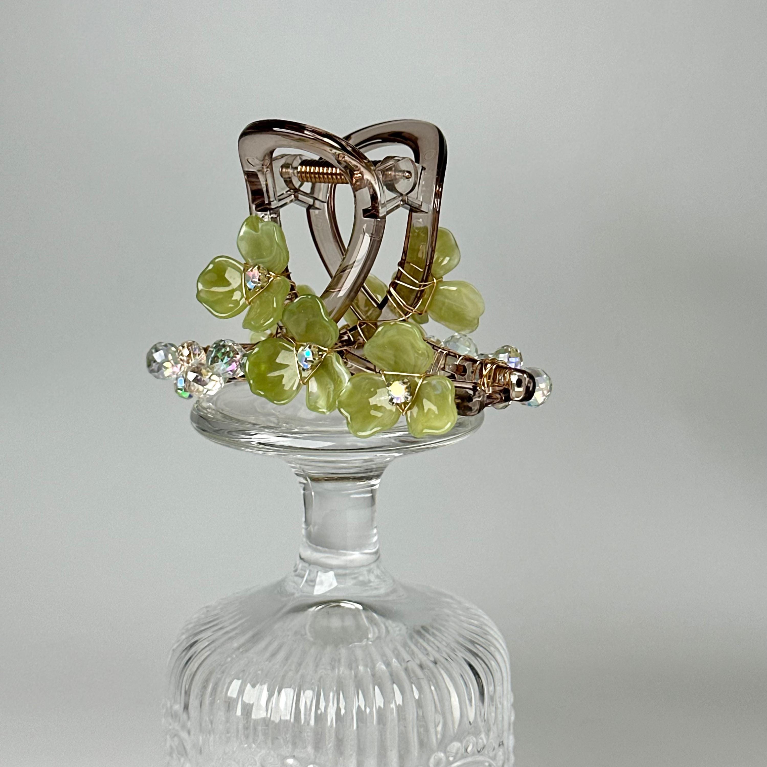 A clear glass vase with a decorative green and silver floral arrangement on top.