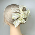 A mannequin head with a blonde wig styled in a bun, adorned with a decorative hair accessory featuring a floral pattern and white lace elements.