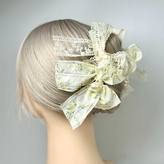 A mannequin head with a blonde wig styled in a bun, adorned with a decorative hair accessory featuring a floral pattern and white lace elements.