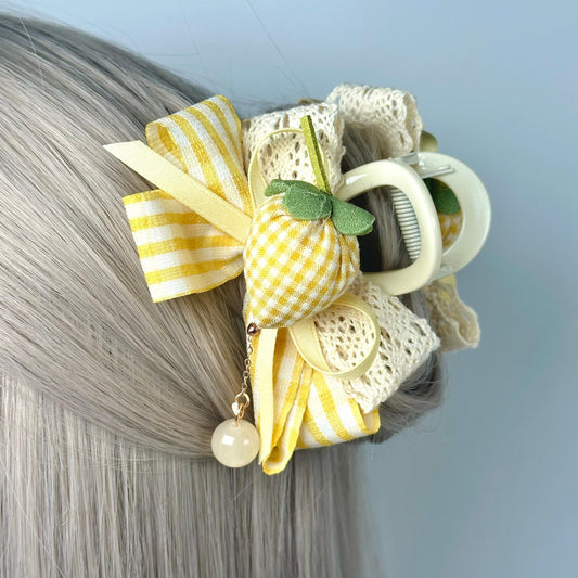 A close-up of a person&#39;s blonde hair with a decorative hair accessory featuring a yellow and white striped ribbon, a green leaf, and a pearl bead.