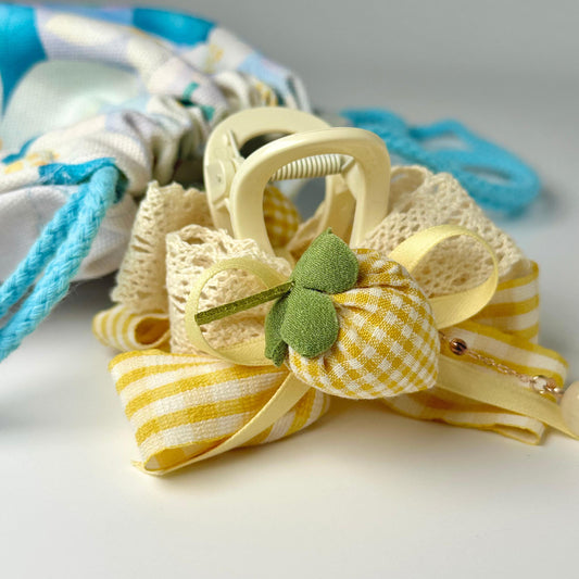 A yellow and white checkered bow tie with a green leaf, tied with a yellow ribbon, is displayed on a white surface.