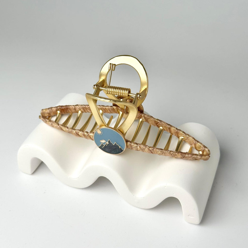 a gold and blue brooch sitting on top of a white stand