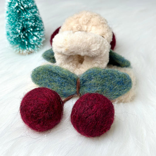 a teddy bear with two balls of yarn next to a christmas tree