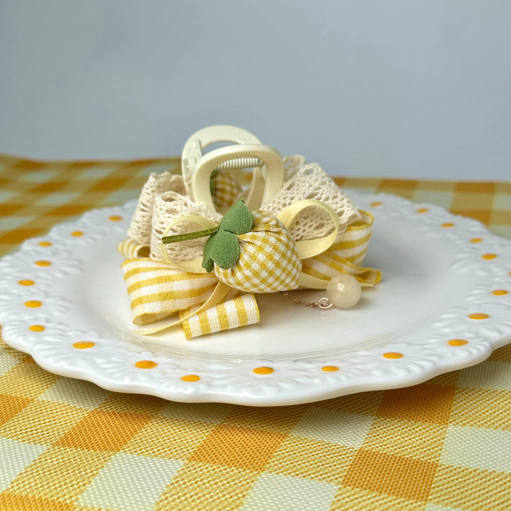 A decorative plate with a yellow and white checkered pattern, featuring a bow made of fabric and ribbons, and a small white charm.