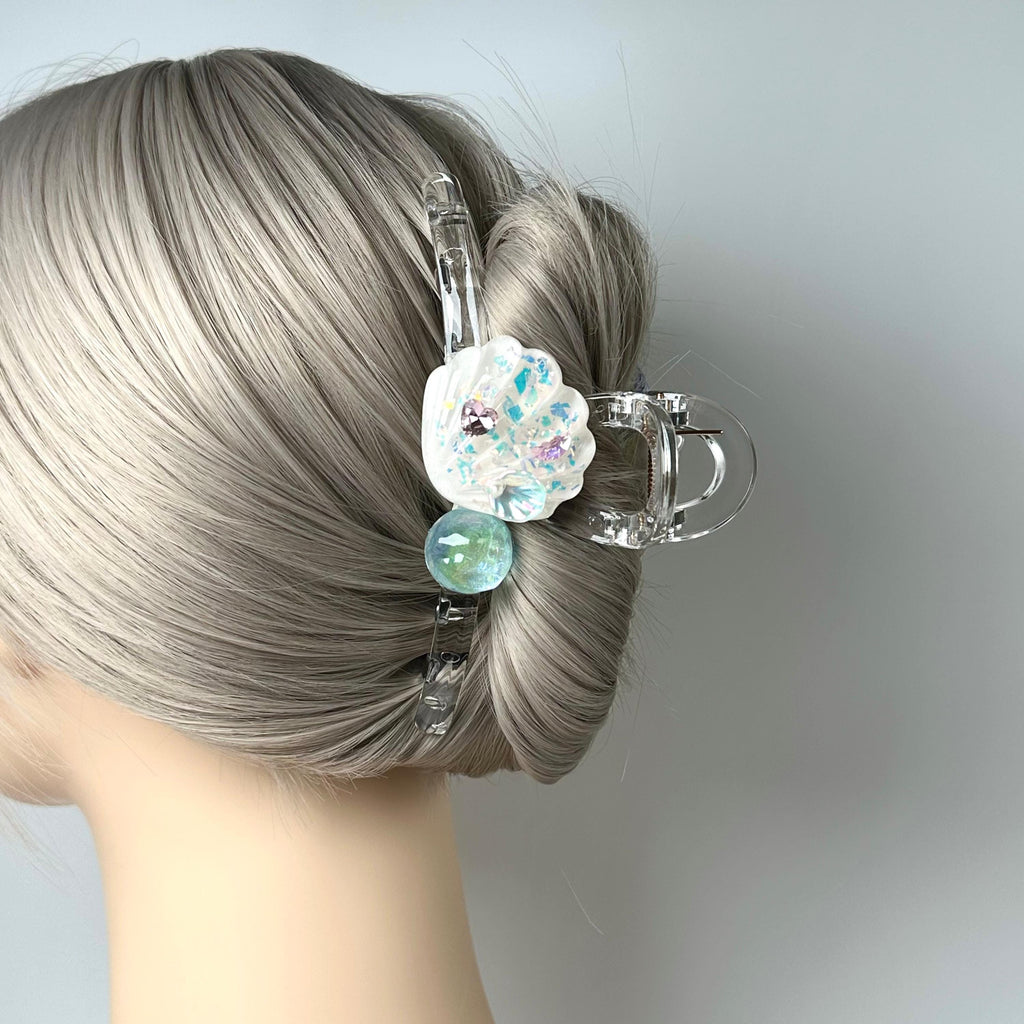 A close-up view of a person's head with a hair clip featuring a flower design and a small green ball.