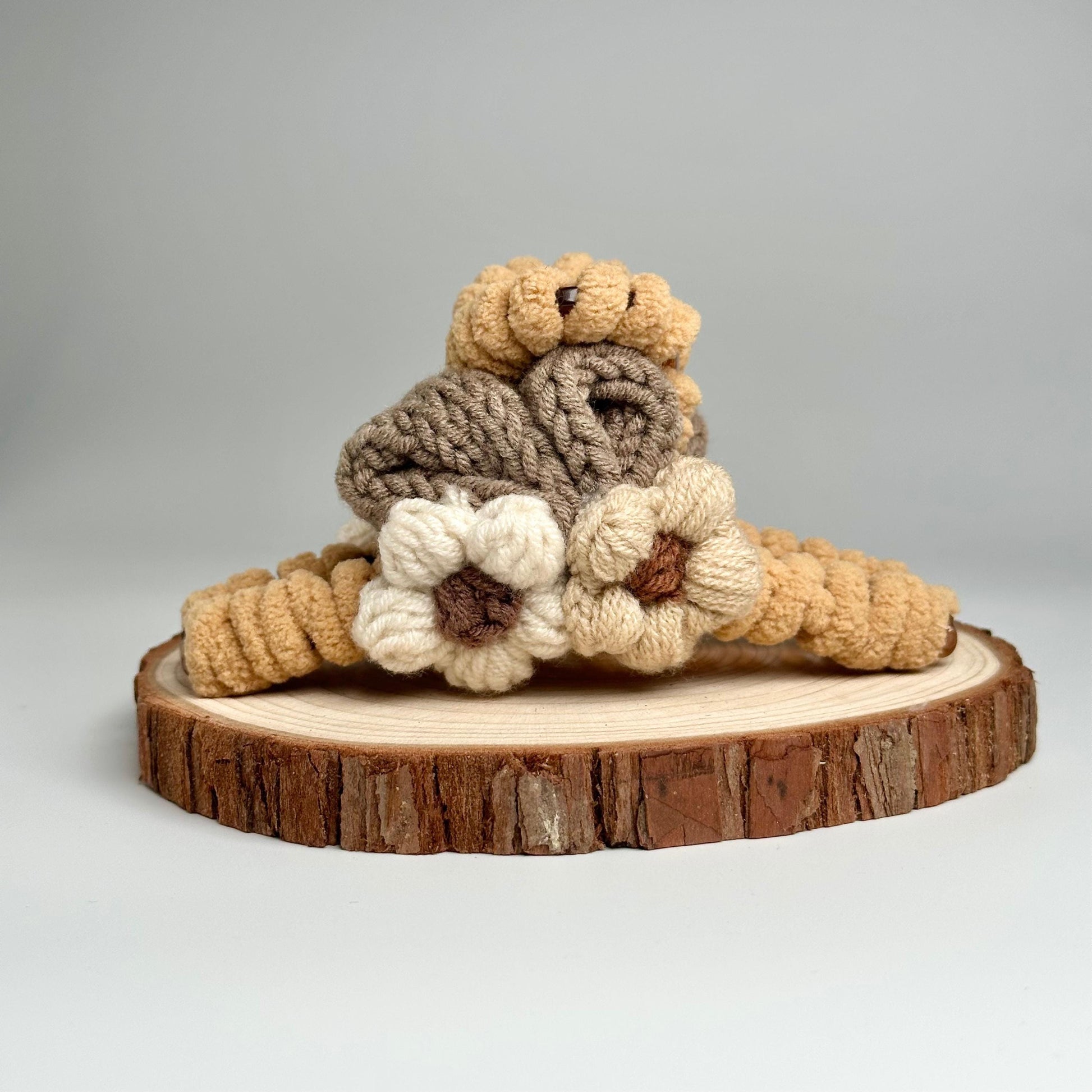 a crocheted teddy bear sitting on top of a piece of wood