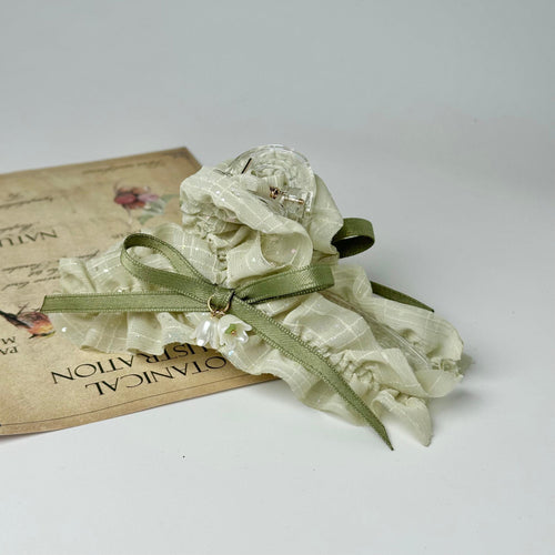 A delicate green ribbon with a clear gemstone is tied around a white fabric, resting on a piece of paper with text.
